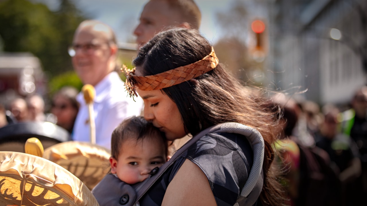 Woman holding baby and kissing its head in a crowd